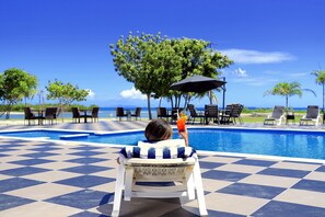 Un espace aménagé au bord de la piscine, avec un sol à carreaux, des chaises longues et une vue sur l’océan.