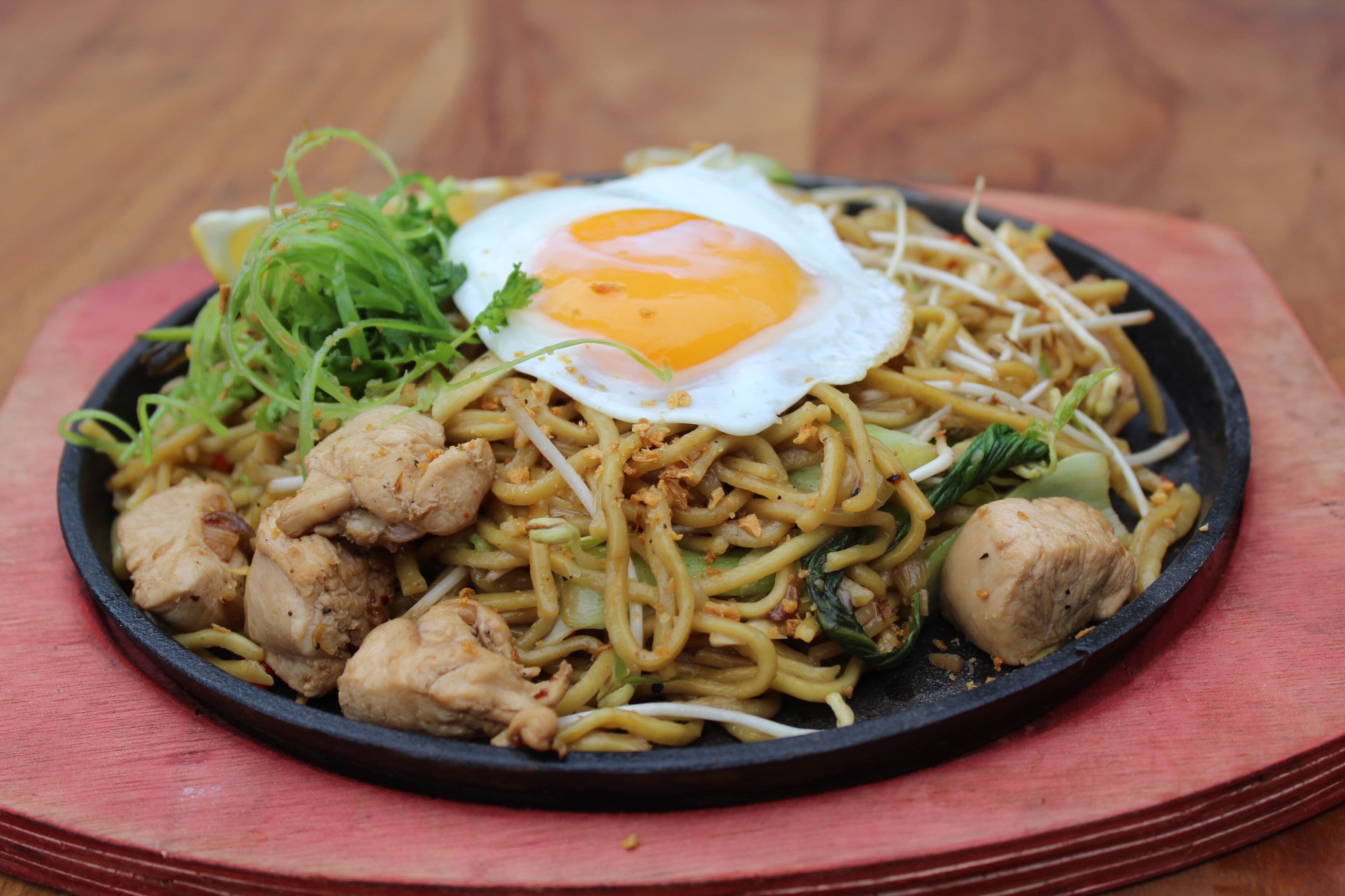 A plate of stir-fried noodles with vegetables and a fried egg on top.