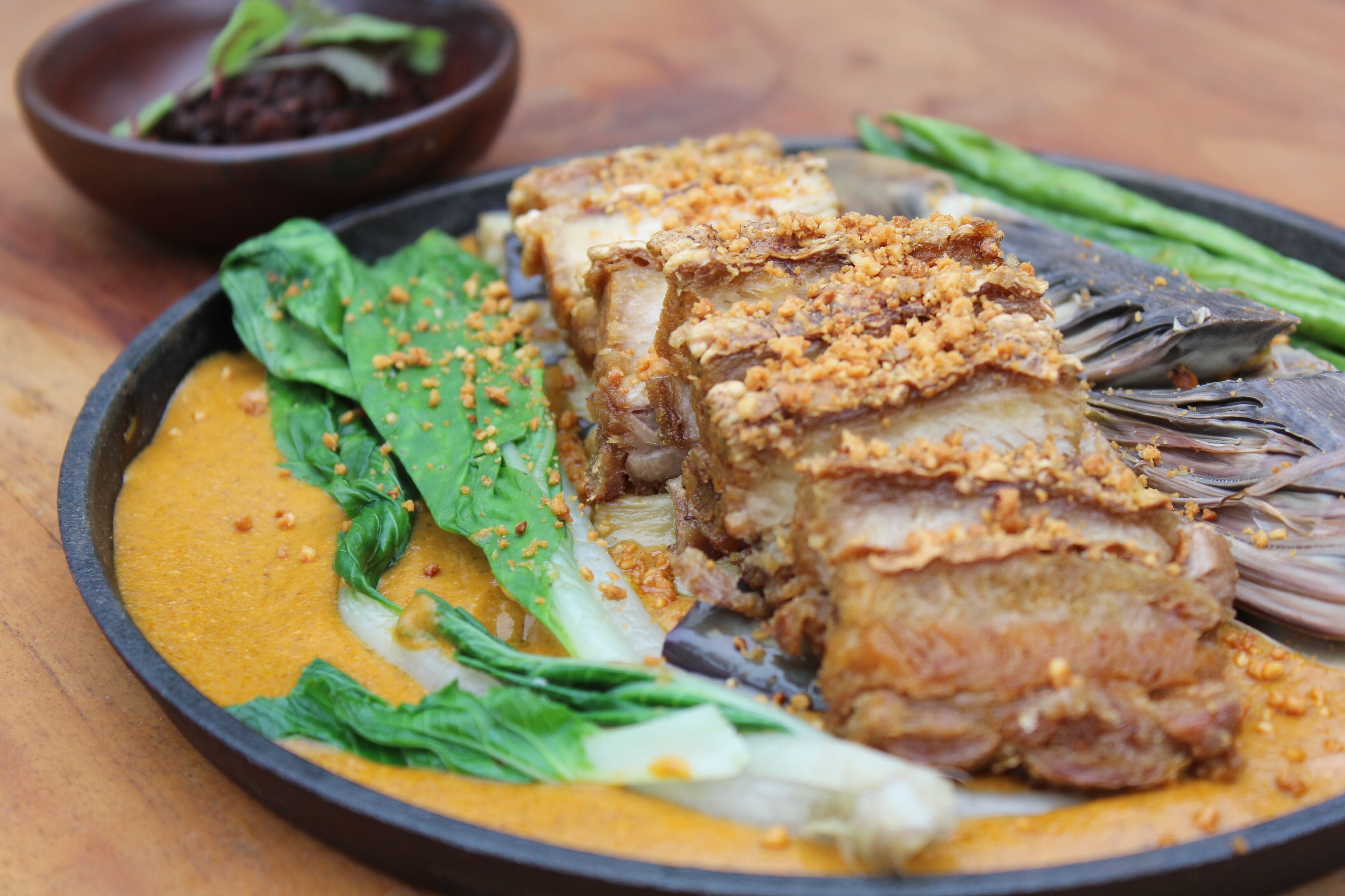 A plate with grilled pork belly, green vegetables, and a yellow sauce.