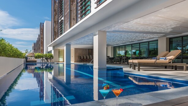 A modern hotel pool area with a clear view of the pool, lounge chairs, and a bar area.