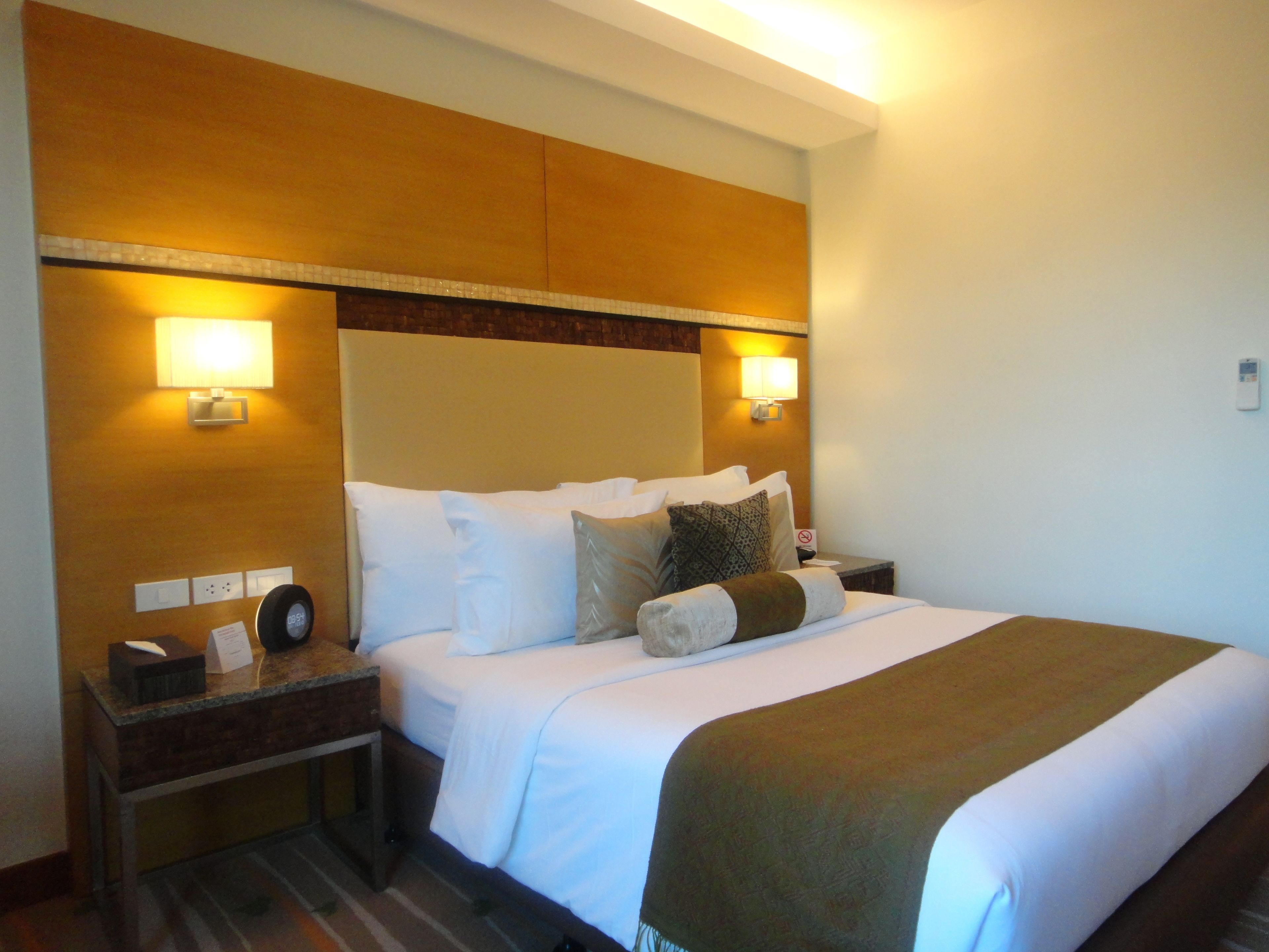 Habitación de hotel con una cama grande, dos mesitas de noche y dos lámparas de pared.