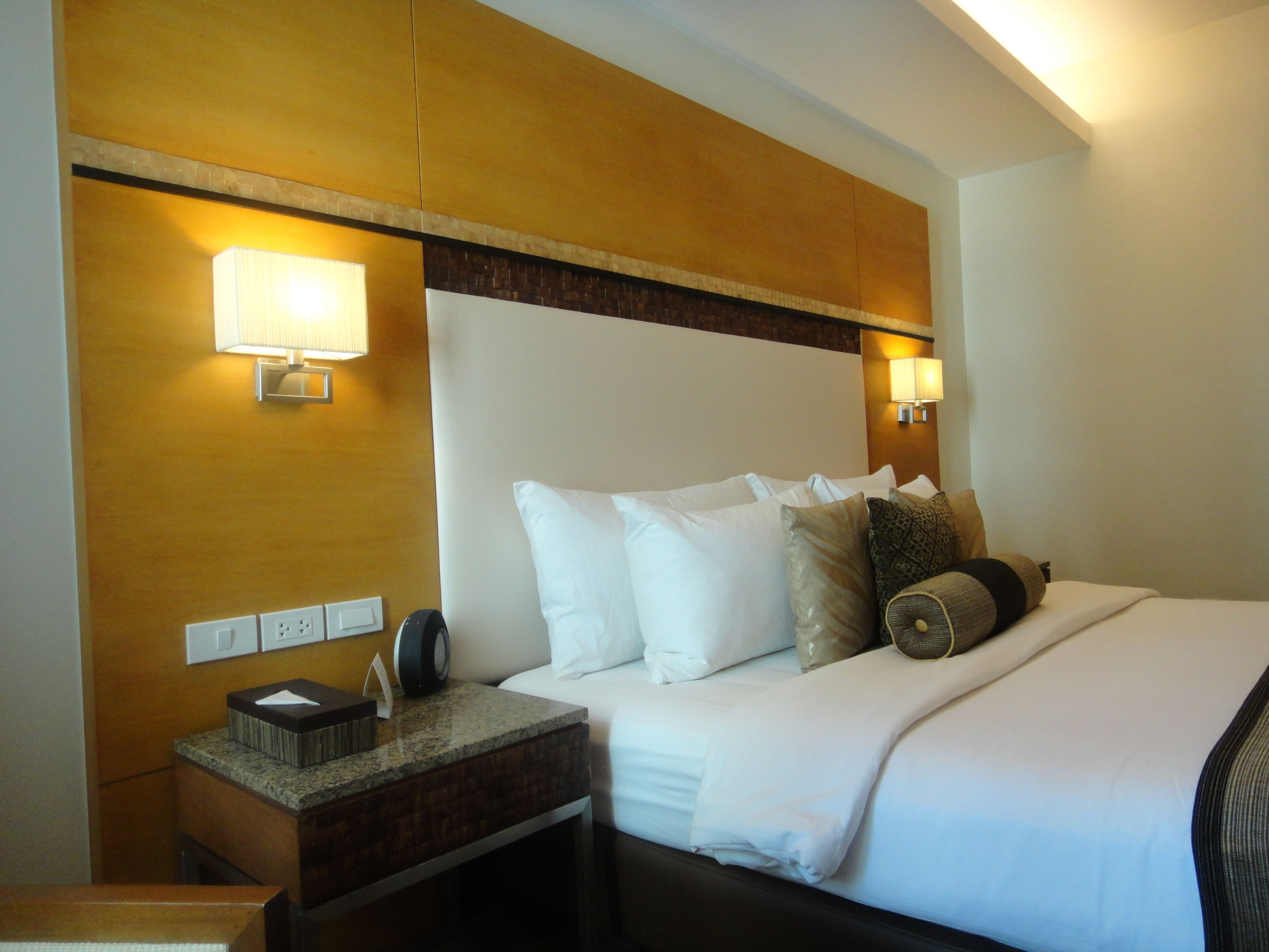 Una habitación de hotel con una cama grande, dos lámparas de noche, una mesita de noche con teléfono y una lámpara de pared.