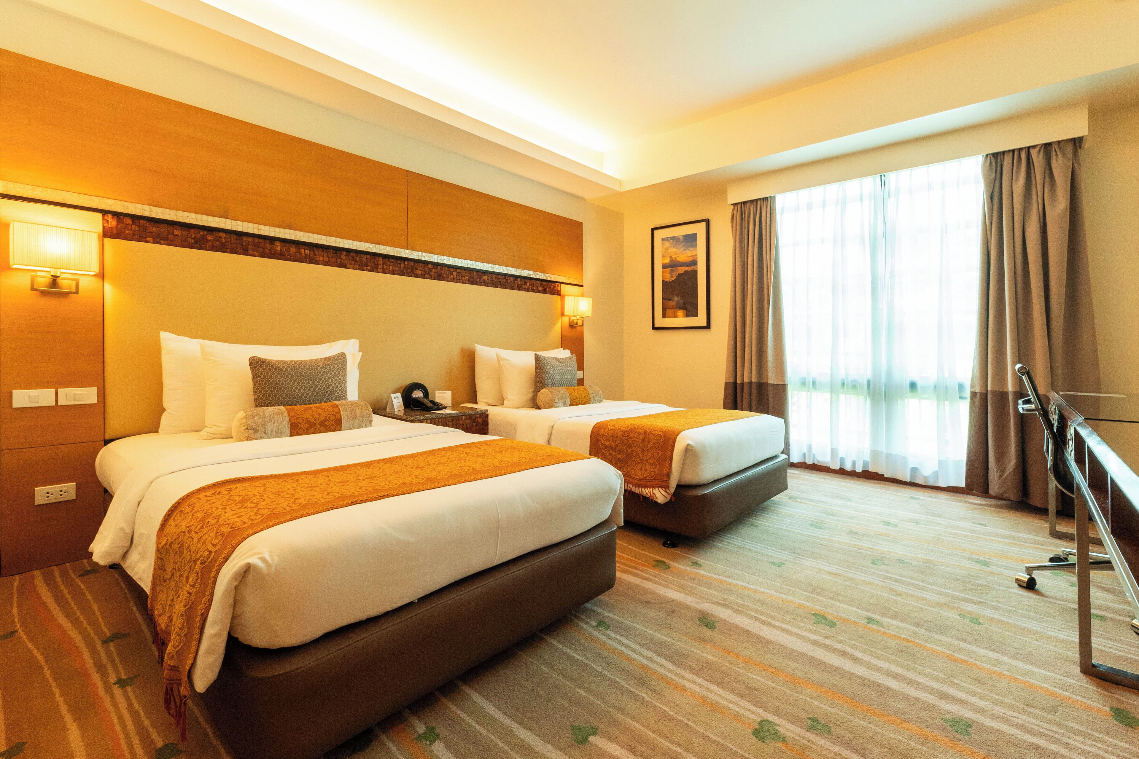 A hotel room with two beds, a large window with curtains, a wooden headboard, and a carpeted floor.