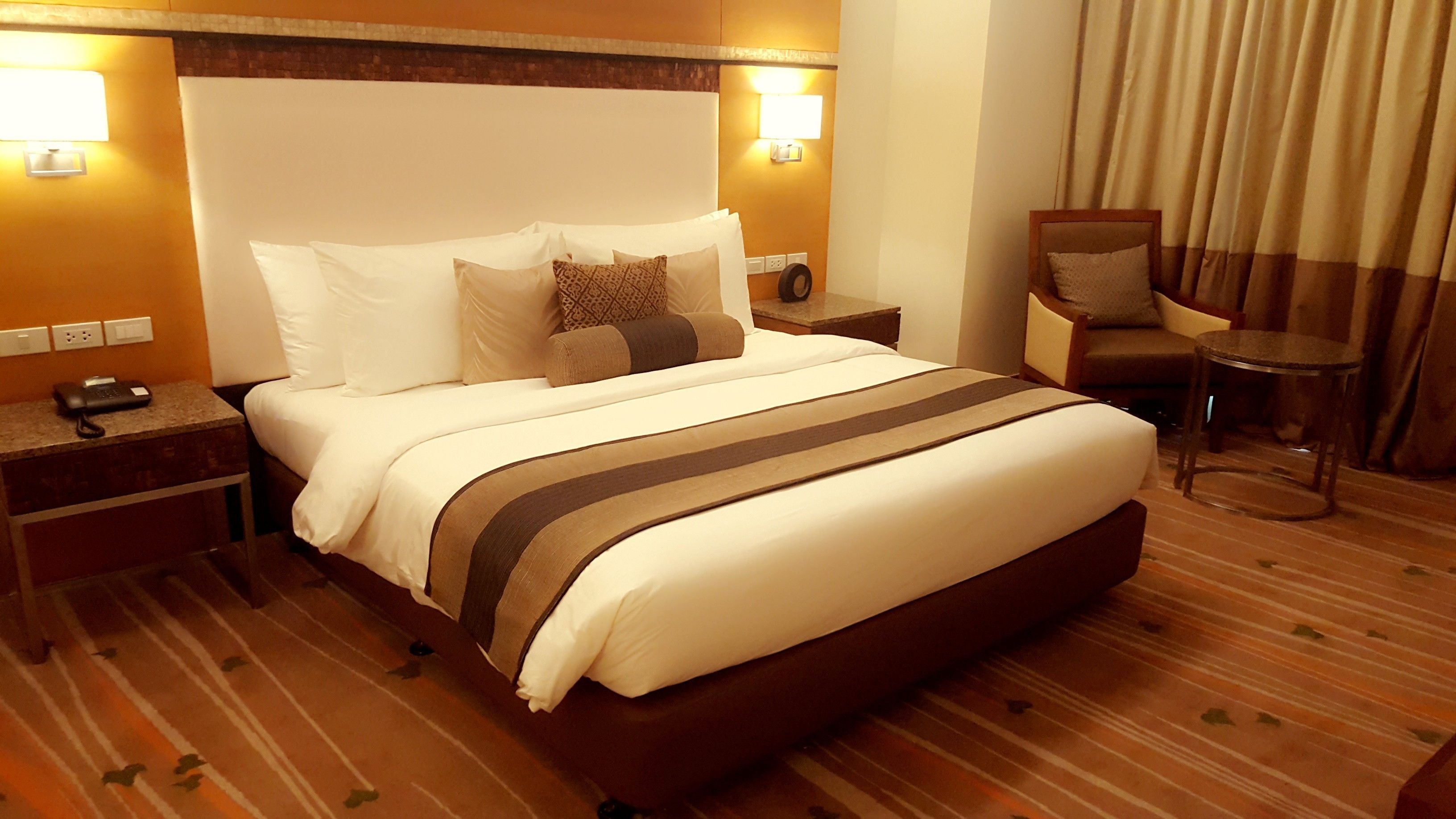 A hotel room with a large bed, a nightstand, a chair, a small table, and a lamp.