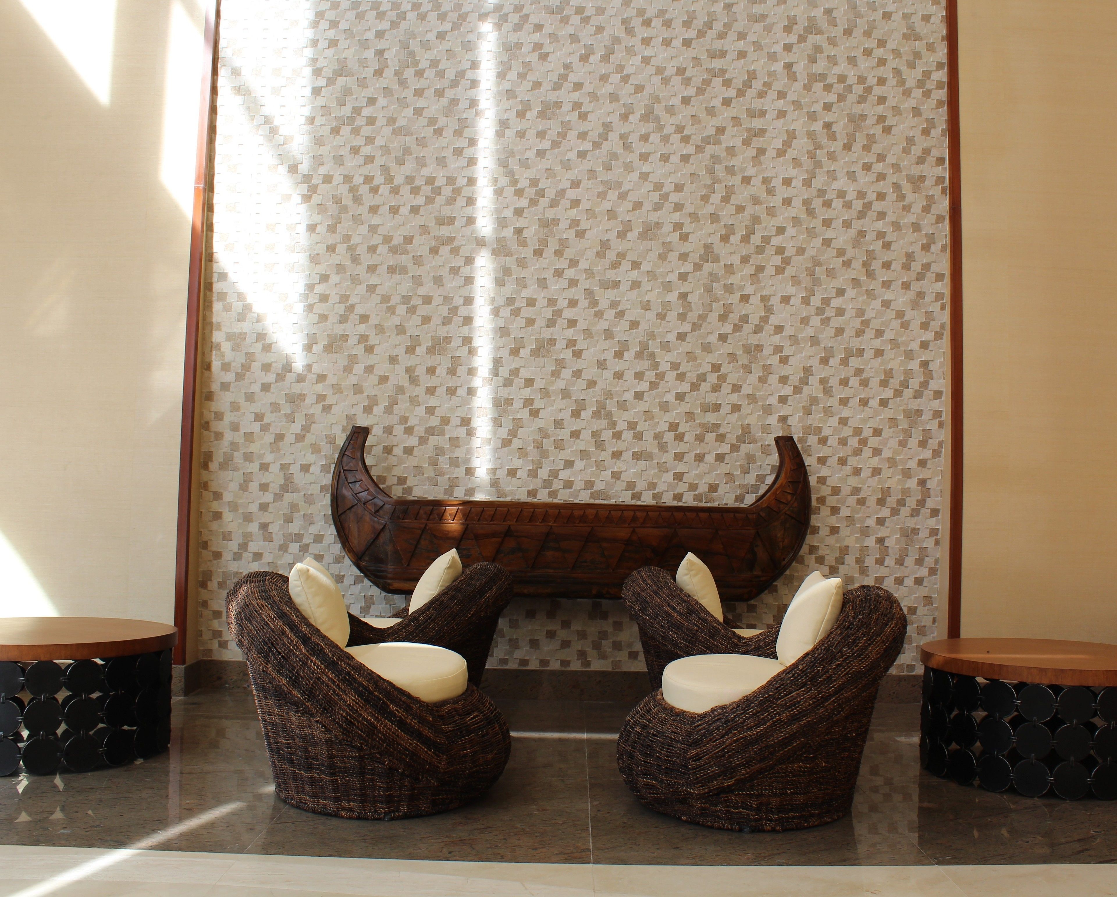 Un intérieur moderne avec deux fauteuils en osier dotés de coussins blancs, un banc en bois au design incurvé et un mur orné d’un motif.