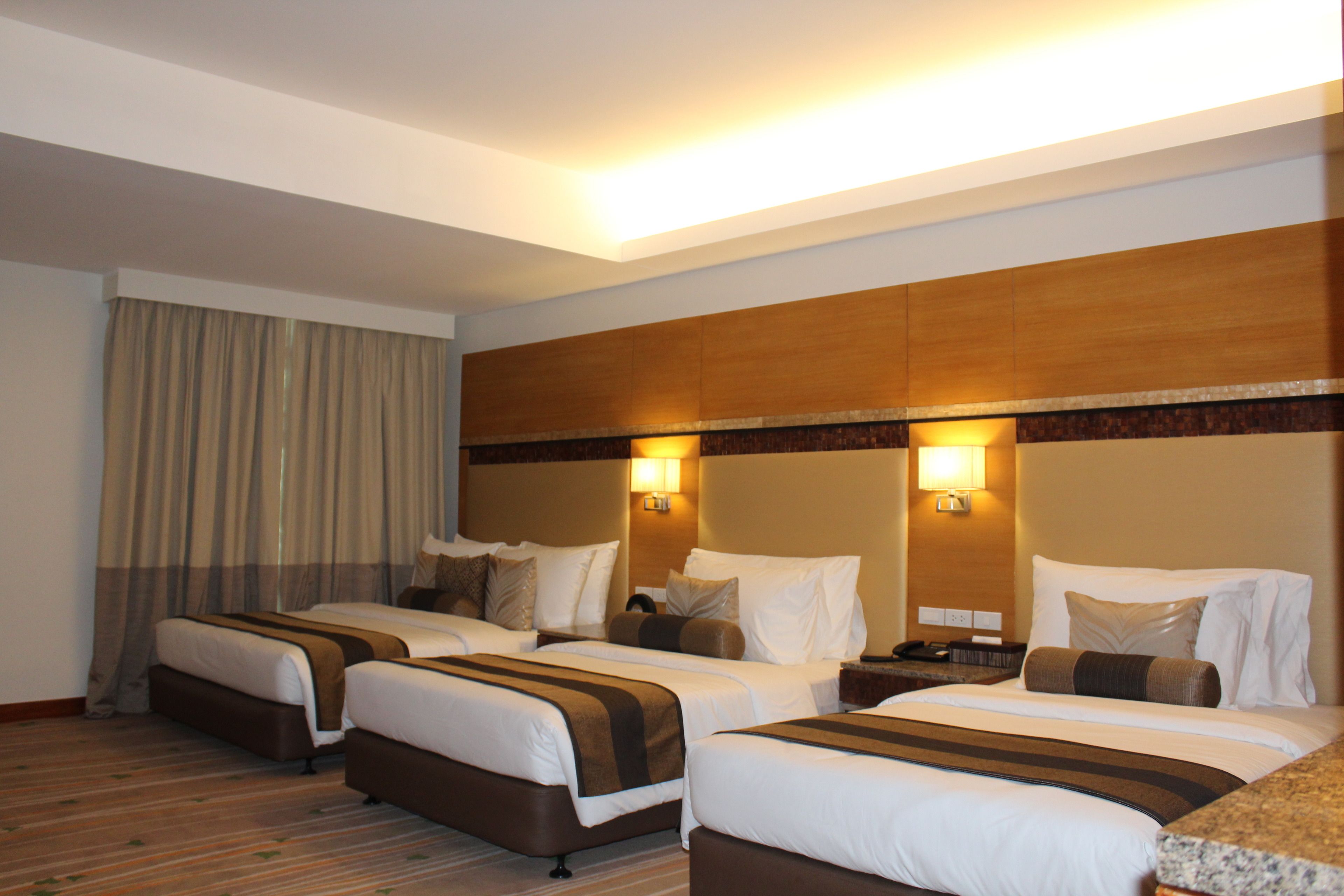 A hotel room with three beds, a wooden headboard, and a large window with curtains.