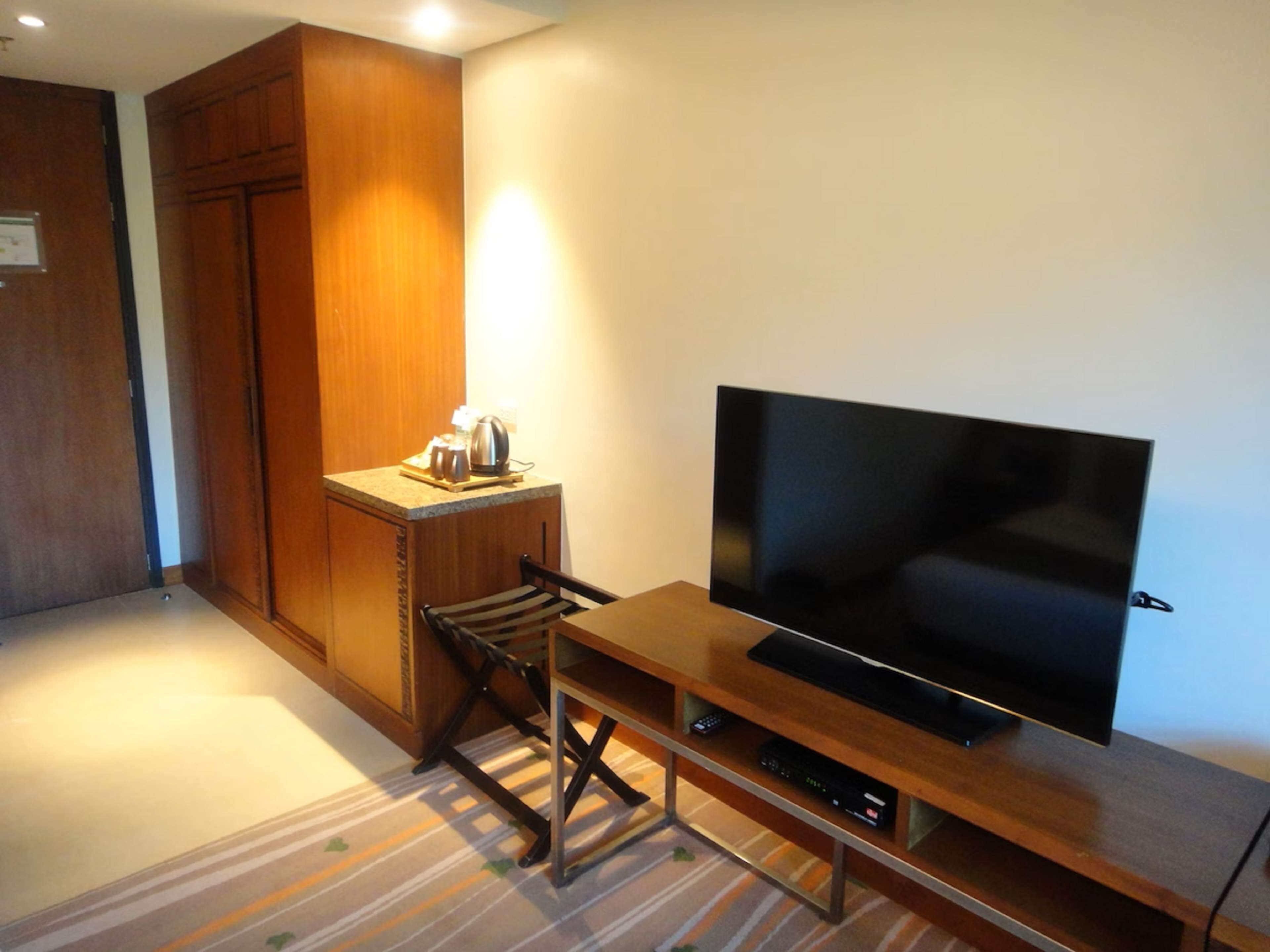 A compact room with a wooden cabinet, a small kitchenette, a television on a wooden stand, and a striped carpet.