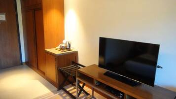 A compact room with a wooden cabinet, a small kitchenette, a television on a wooden stand, and a striped carpet.