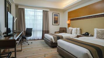 A hotel room with two beds, a desk, a chair, a TV, and a window with curtains.