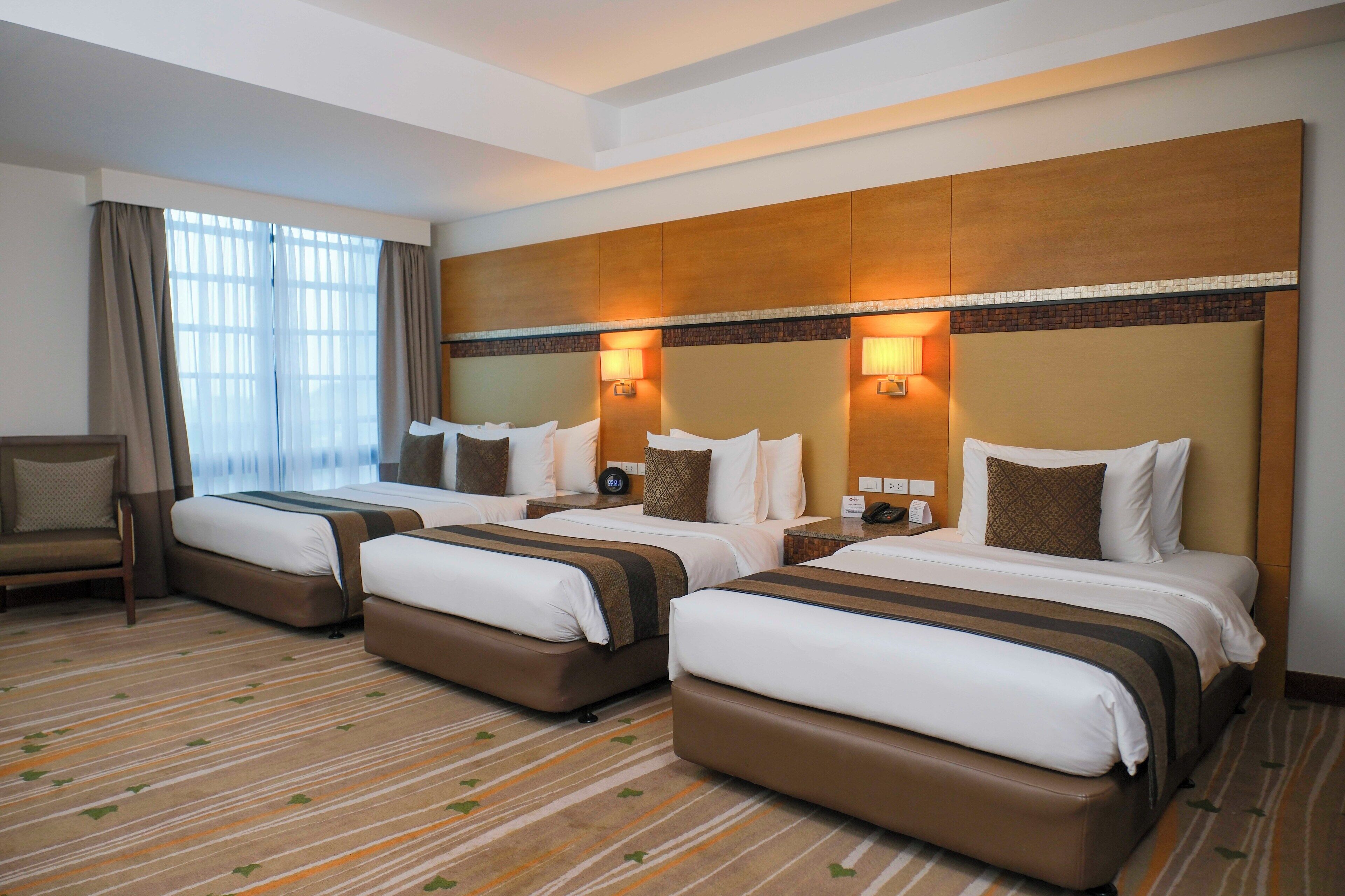A hotel room with three beds, a sofa, and a large window with curtains.