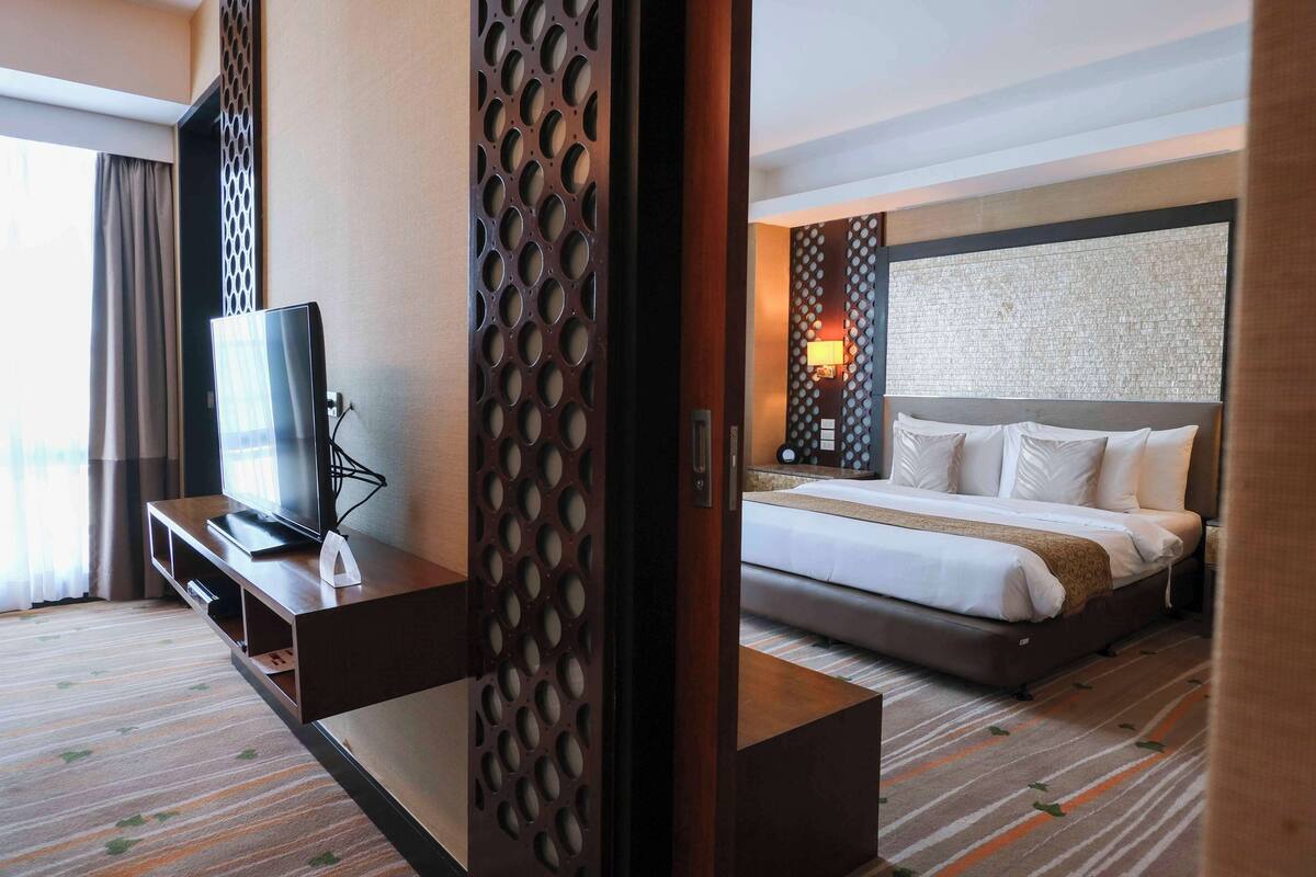Ein Hotelzimmer mit einem Bett, einem Fernseher auf einer Holzkonsole, einer Wand mit Muster und einem Fenster mit Vorhängen.