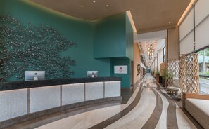Un vestíbulo de hotel moderno con una recepción, un muro decorativo y un largo pasillo que conduce a otras áreas.