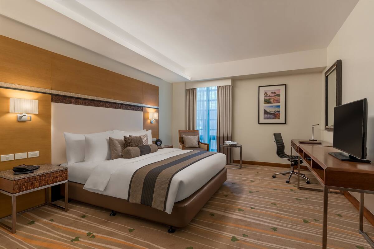Ein Hotelzimmer mit einem großen Bett, einem Schreibtisch mit Computer, einem Fernseher und einem Sessel.