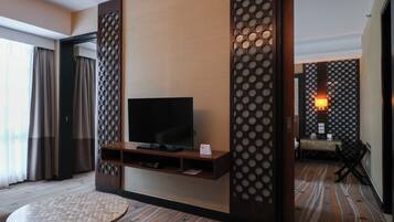A hotel room with a flat-screen TV on a wooden stand, a small round table, and a decorative wall panel.