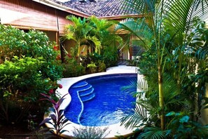 A swimming pool surrounded by lush greenery and a building with a tiled roof. - Hotel Casa Cubana (Granada)