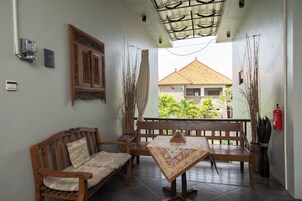 Un balcón con una banca de madera, una mesa con mantel estampado y vista a un edificio con tejado de azulejos.