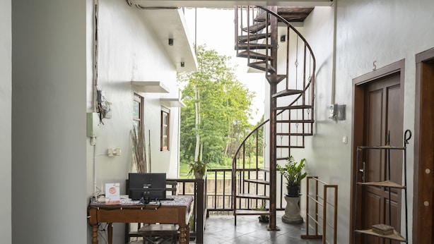 A modern interior with a spiral staircase, a wooden desk with a computer, and a potted plant. - OYO 2417 Panen House (Denpasar)