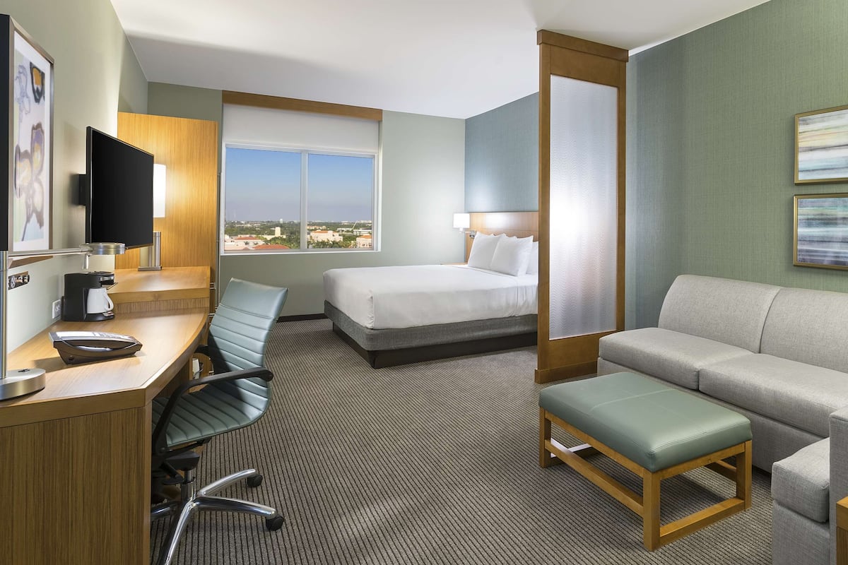 A hotel room with a desk, two beds, a sofa, a coffee maker, and a TV.
