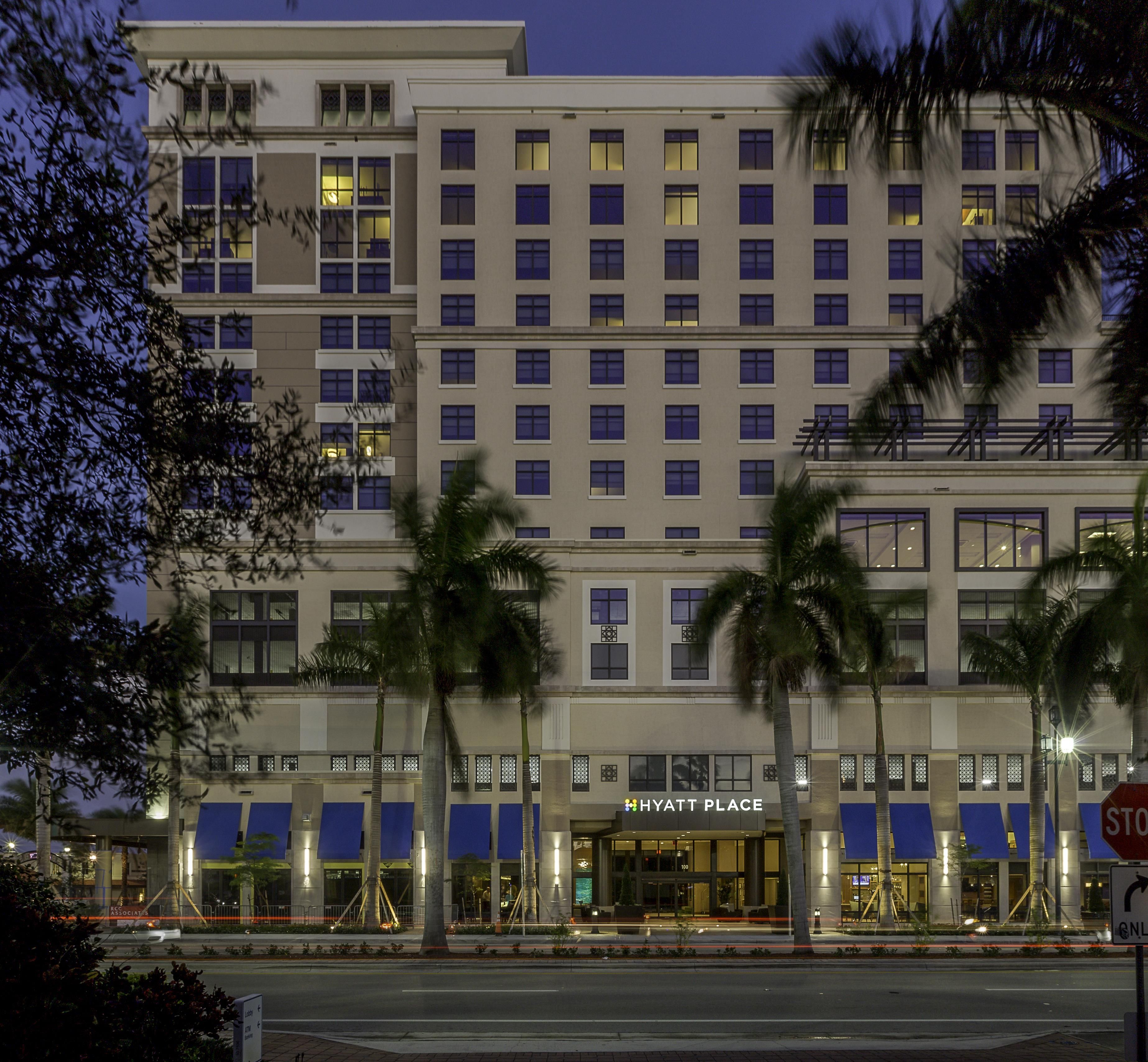 A multi-story hotel with a prominent entrance, palm trees in front, and illuminated windows.