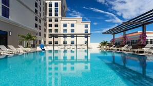 Une piscine d’hôtel avec une eau d’un bleu limpide, des chaises longues et un bâtiment à plusieurs étages doté de balcons.