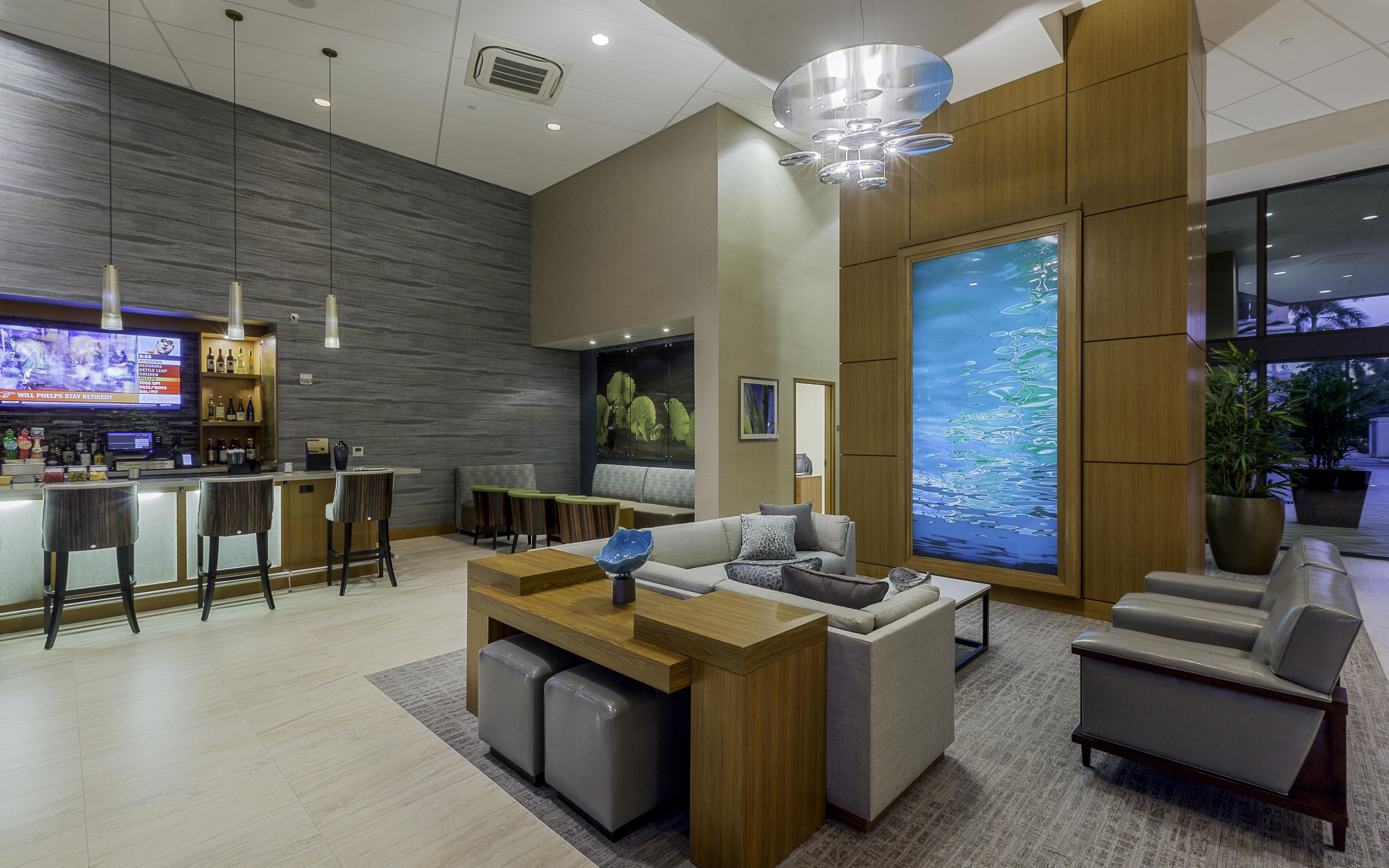 A modern lobby with a bar area, seating, and a large digital screen.