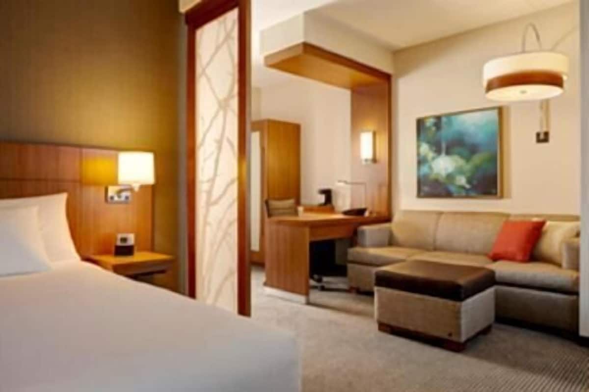 A hotel room with a bed, a desk, a sofa, and a painting on the wall.
