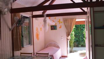A room with a bed, a table with chairs, a fan, and a window with curtains.