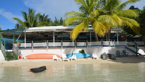 A beachside building with a covered seating area, clear water, and palm trees. - Pension Fare Maheata (Moorea-Maiao)