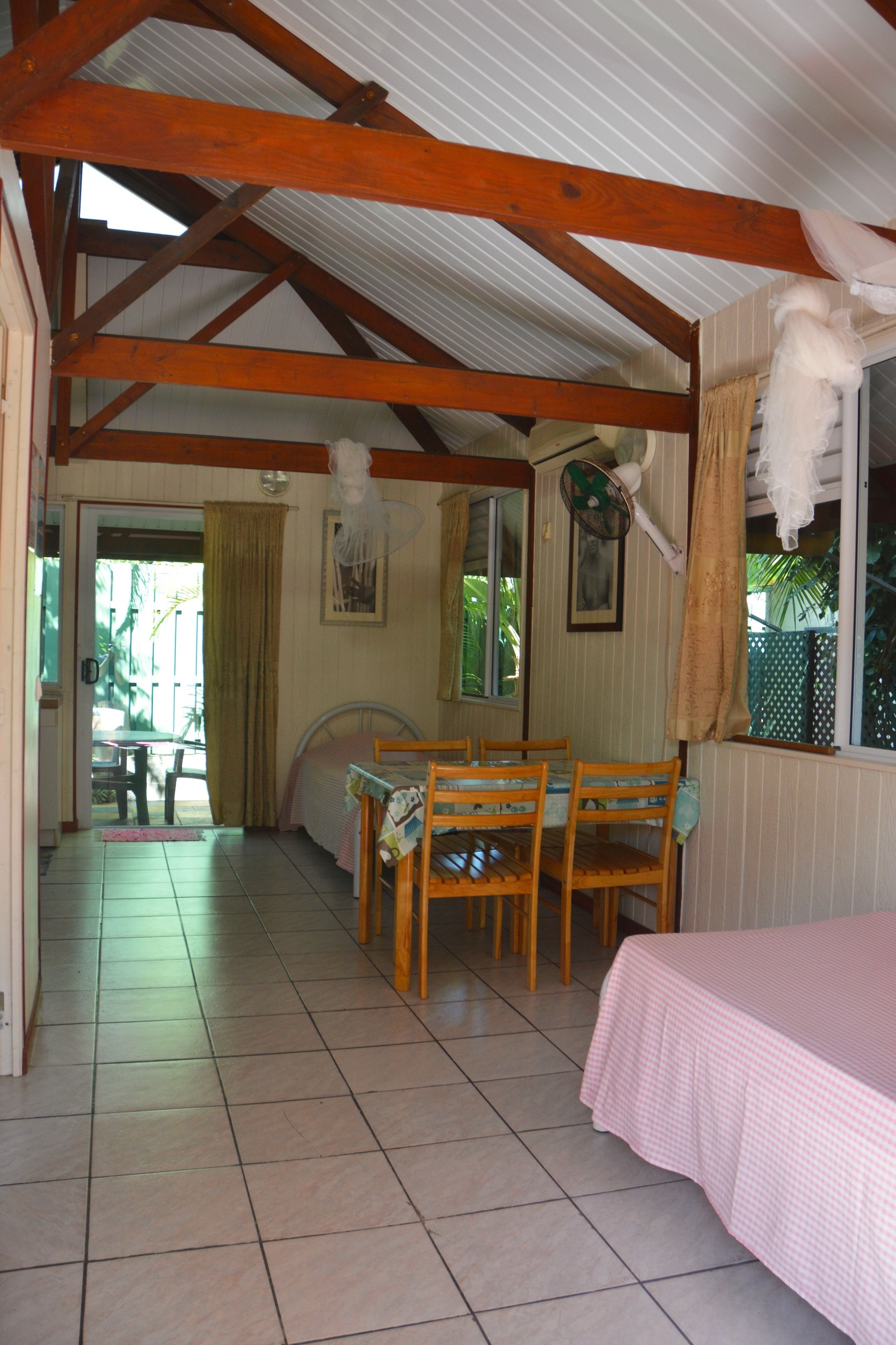 A room with a bed, a dining table with chairs, a window with curtains, and a fan.