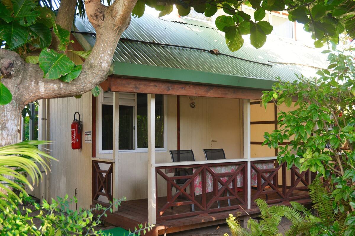 A wooden deck with a railing, a fire extinguisher, and a window overlooking a garden.
