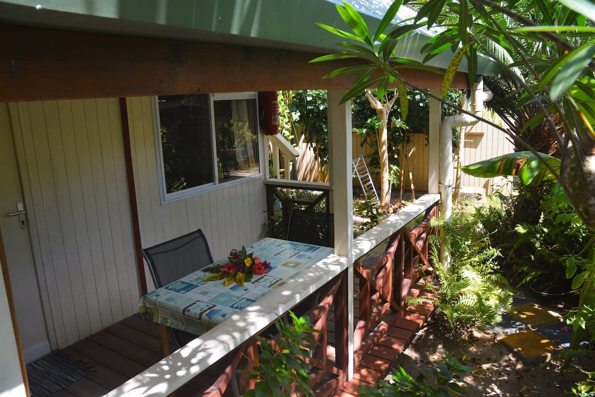 A covered patio with a table set for dining, surrounded by lush greenery and a small water feature.
