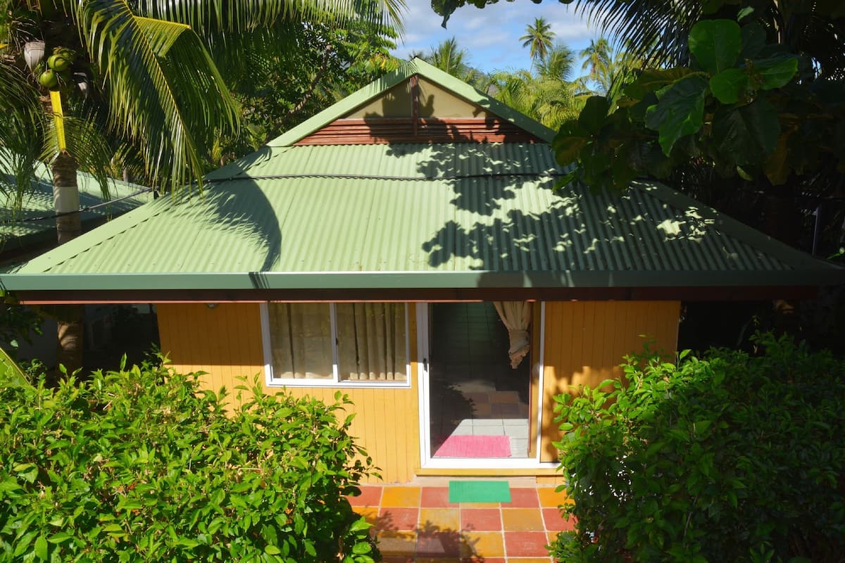 A small house with a green roof, a sliding glass door, and a tiled porch.