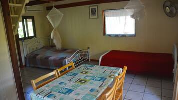 Um quarto com uma cama, uma mesa com cadeiras, um sofá vermelho, uma janela com cortina e um ventilador.