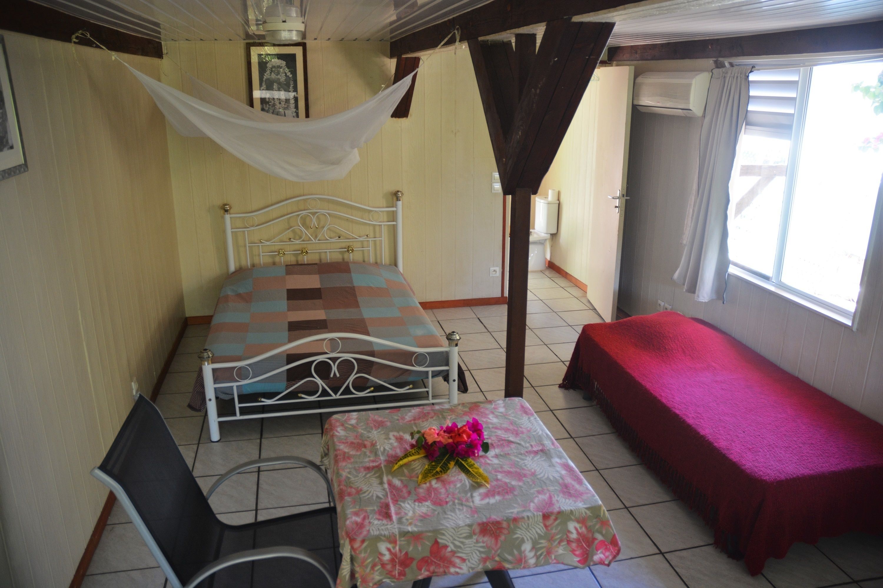 A room with a bed, a small table with a floral tablecloth, a chair, and a bench.