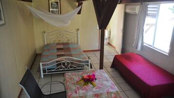 A room with a bed, a small table with a floral tablecloth, a chair, and a bench.