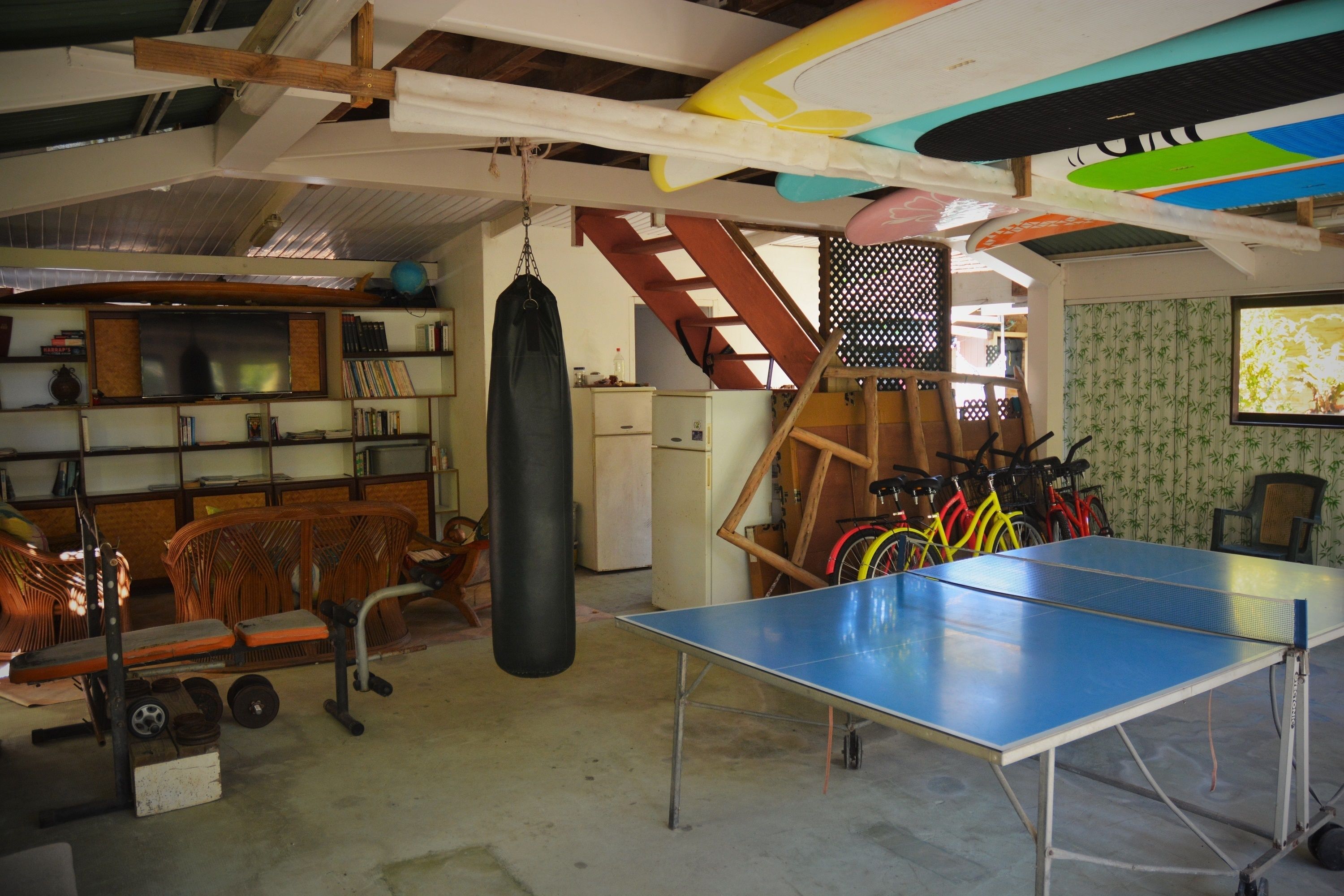 Una habitación con mesa de ping pong, equipo de ejercicio, bicicletas y saco de boxeo.