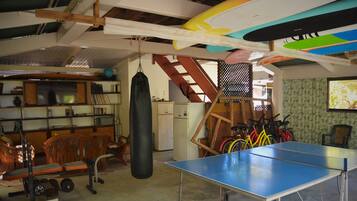 Una habitación con mesa de ping pong, equipo de ejercicio, bicicletas y saco de boxeo.