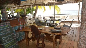 A wooden deck with a table and chairs, overlooking a beach. - Pension Fare Maheata (Moorea-Maiao)