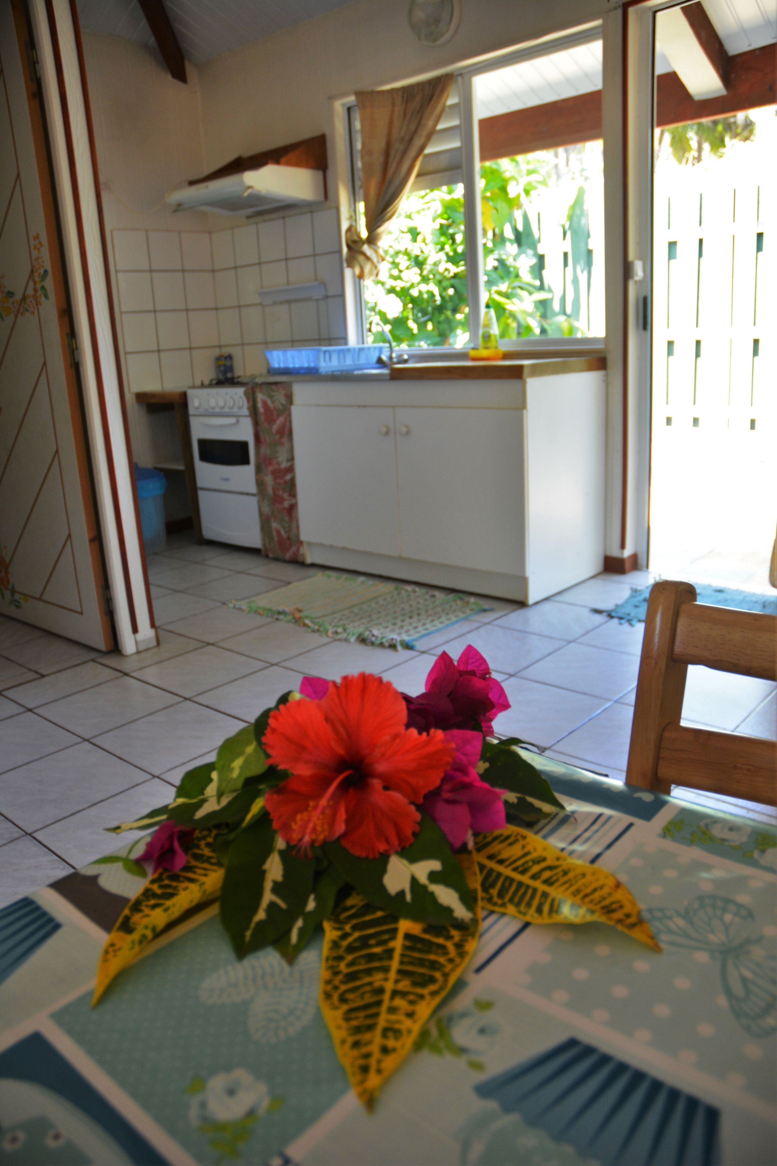 Una cocina con armarios blancos, un ventanal con cortinas y una mesa con un centro de mesa floral.