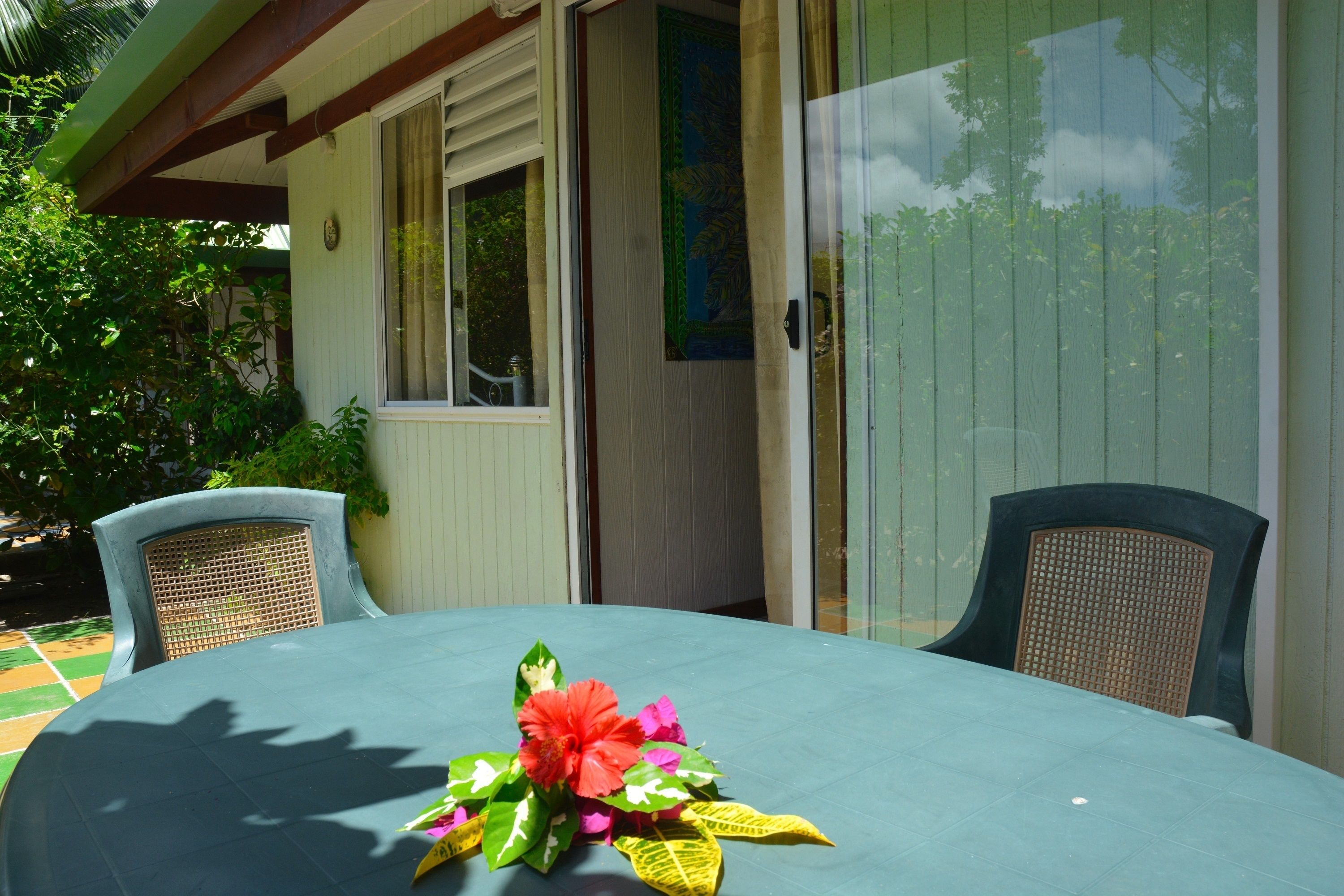 A round table with a floral centerpiece, two wicker chairs, and a sliding glass door leading to a covered outdoor area.