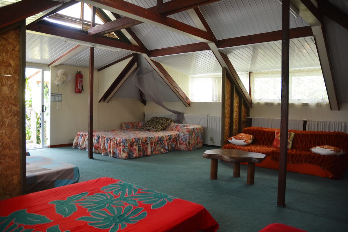 A room with a sloped ceiling, a bed with a floral bedspread, a sofa with an orange blanket, and a small table.