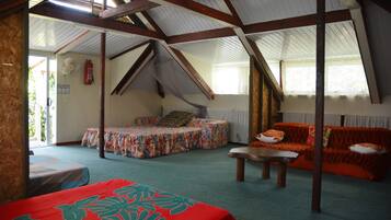A room with a sloped ceiling, a bed with a floral bedspread, a sofa with an orange blanket, and a small table.