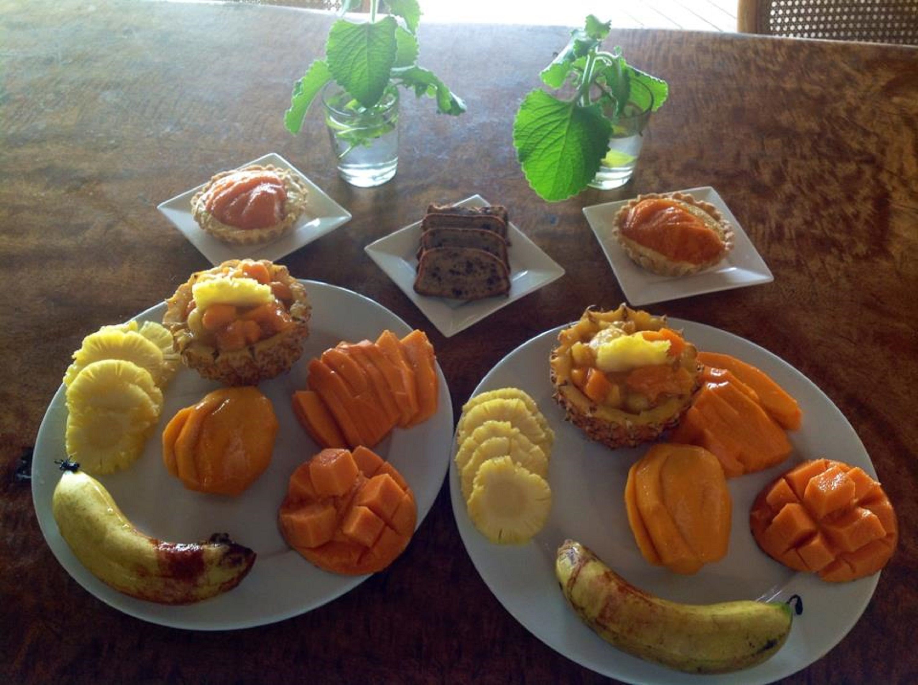 Una mesa con platos de comida, incluyendo plátanos, mangos y pasteles.