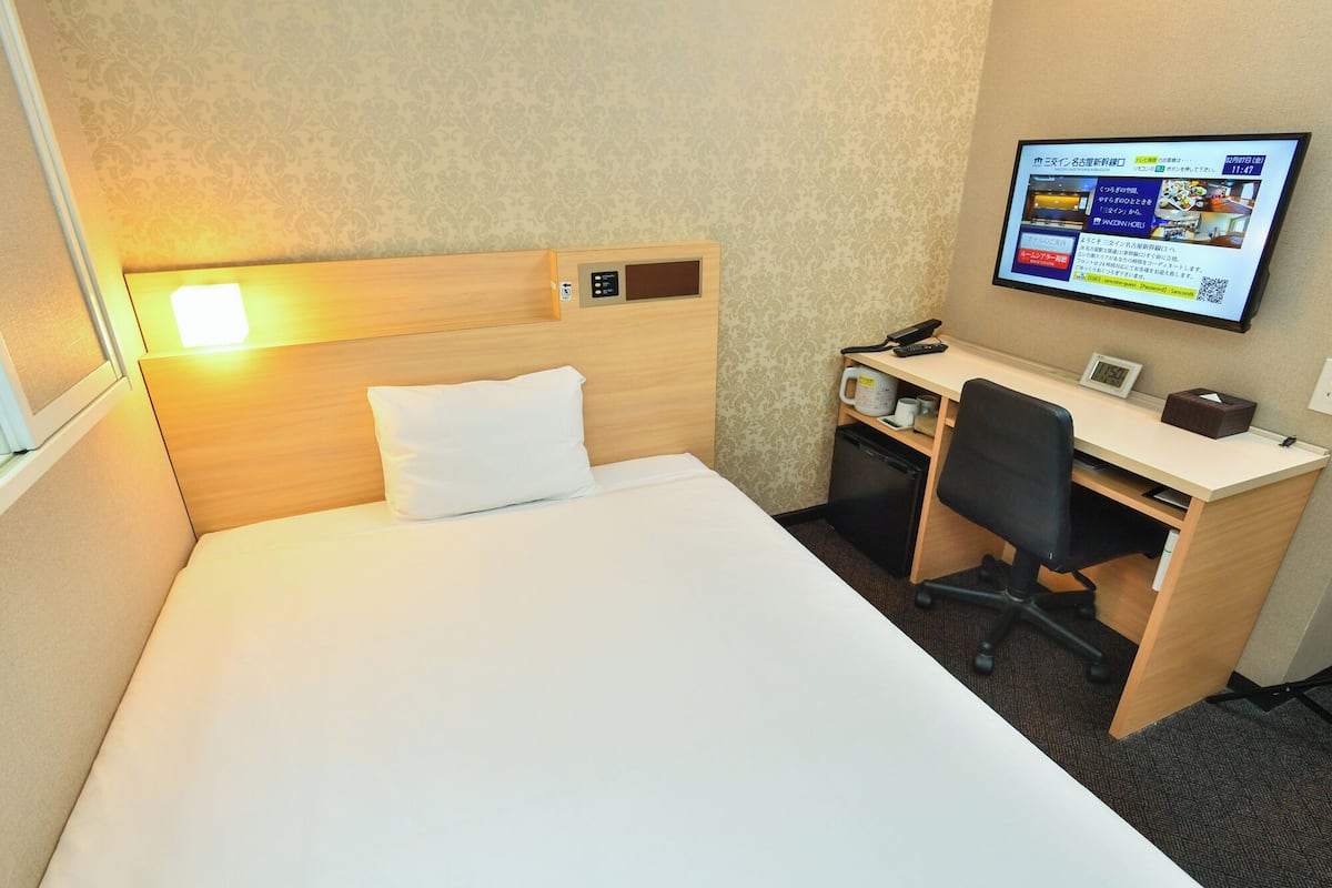 A hotel room with a bed, a desk, a chair, a television, and a clock.