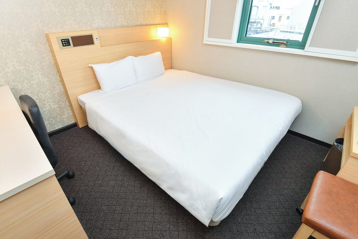 A hotel room with a bed, a desk, a chair, and a window.