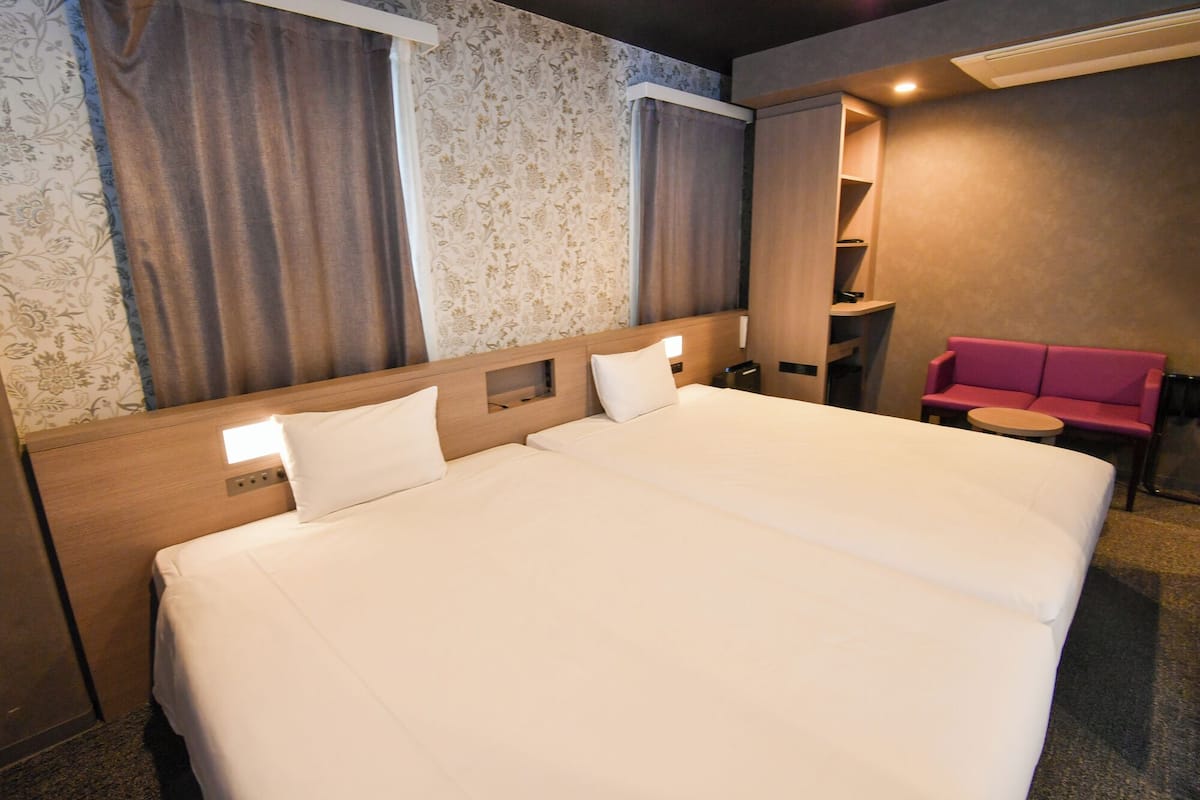 A hotel room with a large bed, a bedside table, a small round table, and a pink sofa.