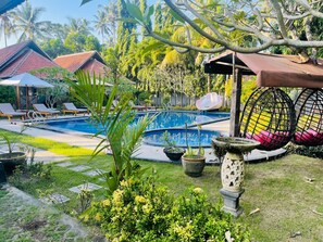 A pool area with lounge chairs, a hot tub, and a garden with potted plants and a bird bath. - Mutiara Bali (Karangasem)