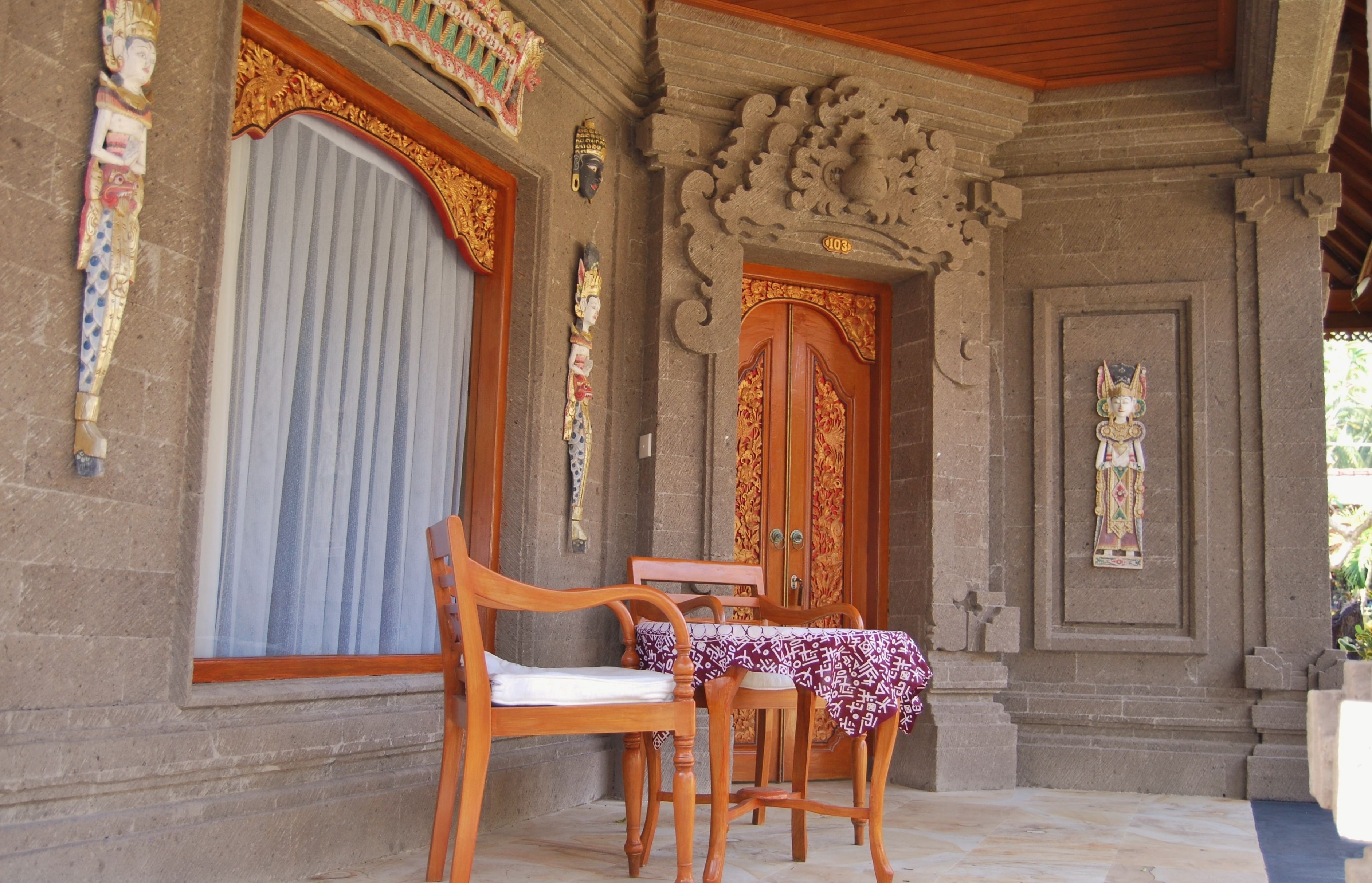 Un edificio tradicional con puertas y columnas de madera ornamentada, un porche cubierto con sillas y una mesa de madera, y el número '403' en la puerta.
