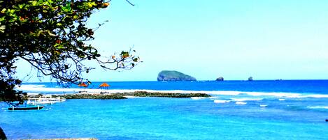 A coastal scene with clear blue water, a small island, and boats.