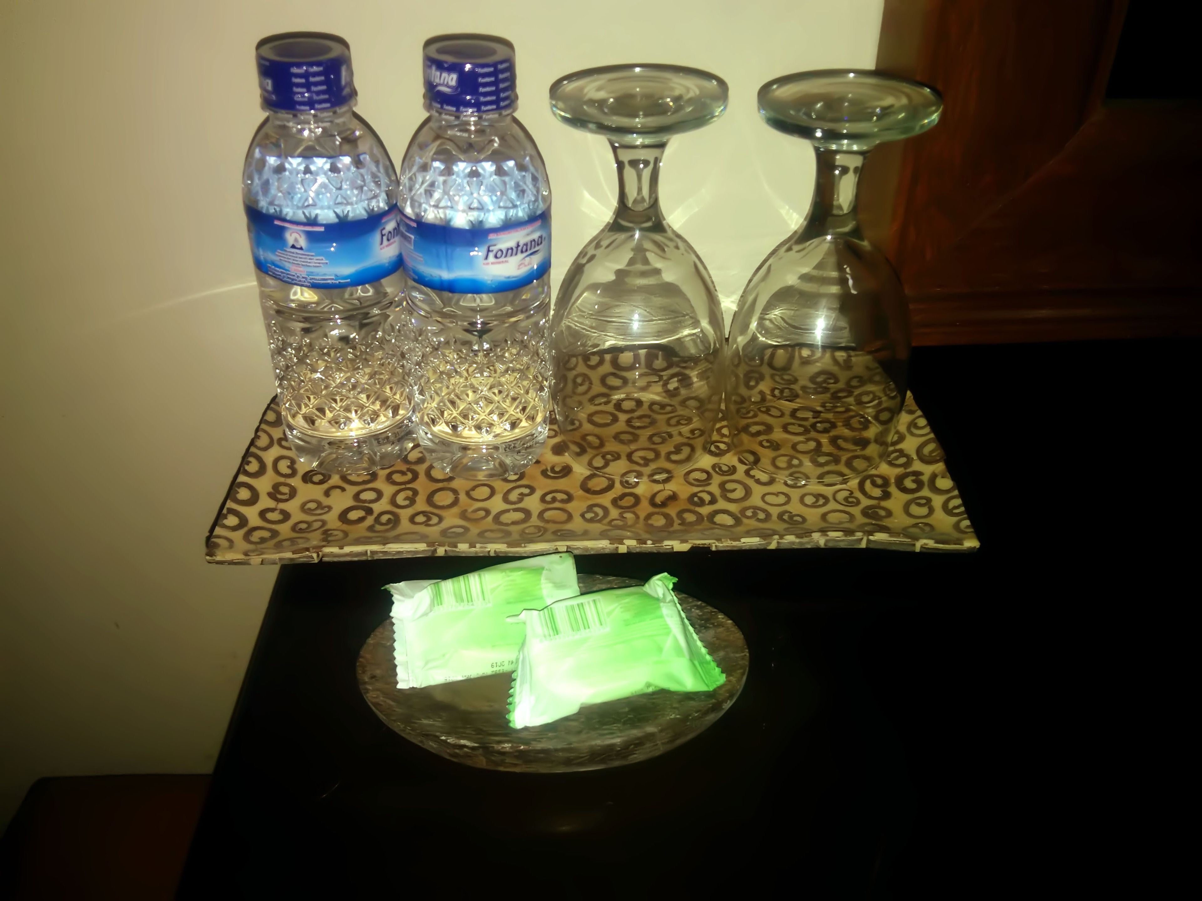 Una bandeja con dos botellas de agua, tres vasos y dos paquetes de refrigerios sobre una mesa.